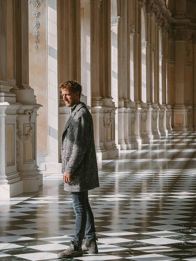 Man standing in a grand Italian building with columns and a checkered floor.