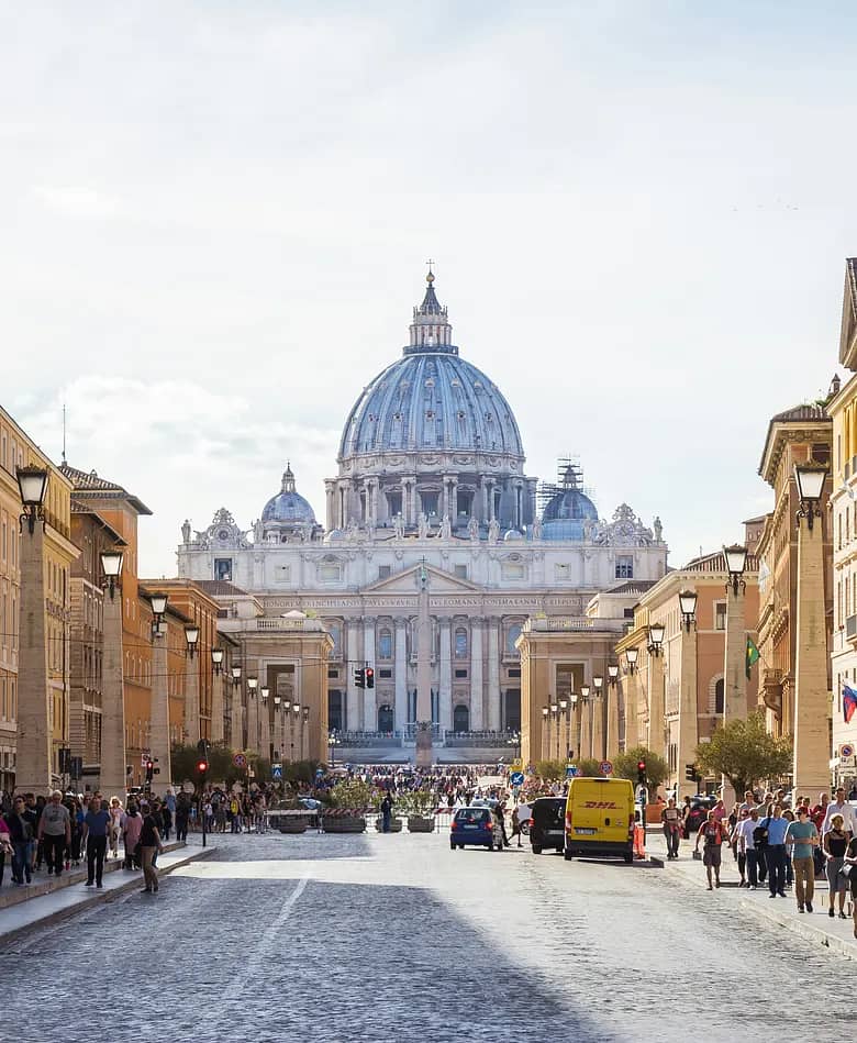 Via della Conciliazione in Rome, lined with lamp posts and pedestrians, leading to the dome of St. Peter's Basilica.